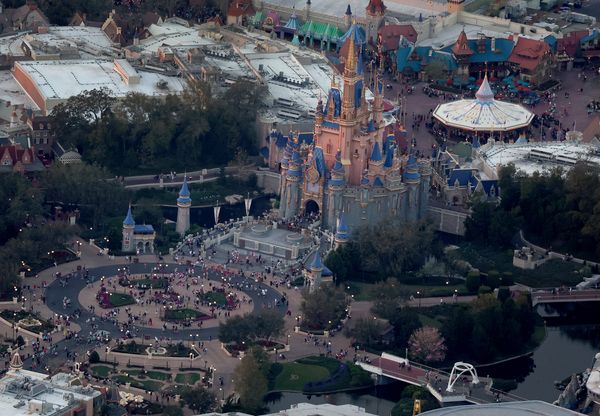 An aerial view of Walt Disney World shows people in the park near a large castle.