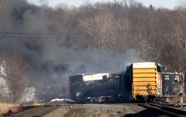 Smoke surrounds a train that is off its tracks. Trees are in front of the train.